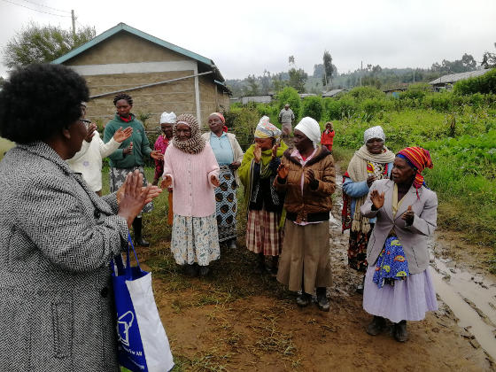 African ladies clapping by a grey building